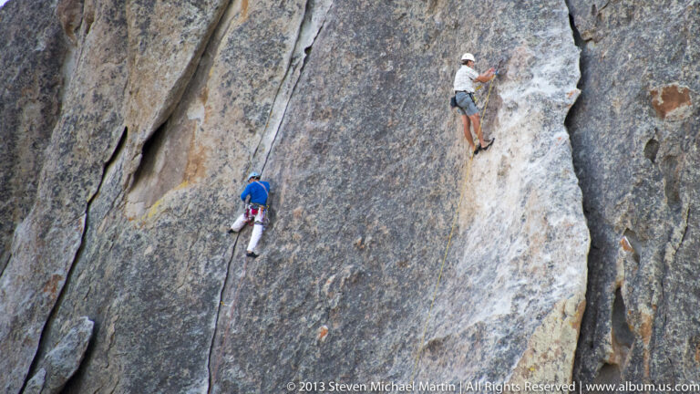 Two climbers use ropes on separate sections of a steep granite slab.