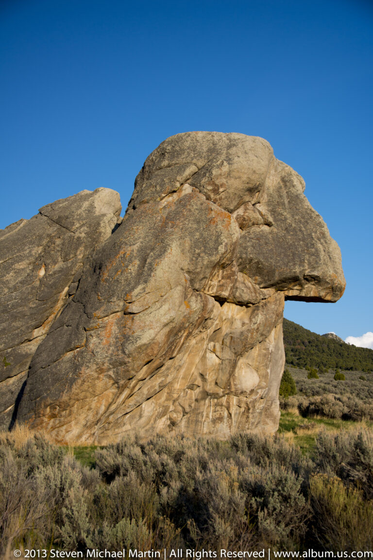 A low granite arch with an overhanging lip stands above open scrubland.