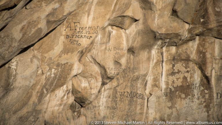 Handwritten names and dates appear across a cracked, warm-colored granite wall.