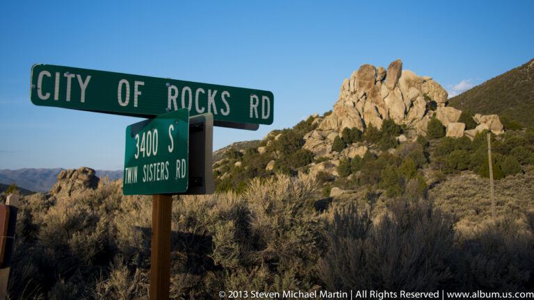 Green City of Rocks Road and Twin Sisters Road signs stand before granite formations.