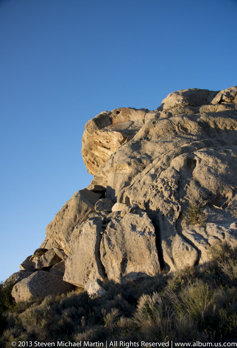 A layered granite ledge with a rounded overhang rises above sparse brush.