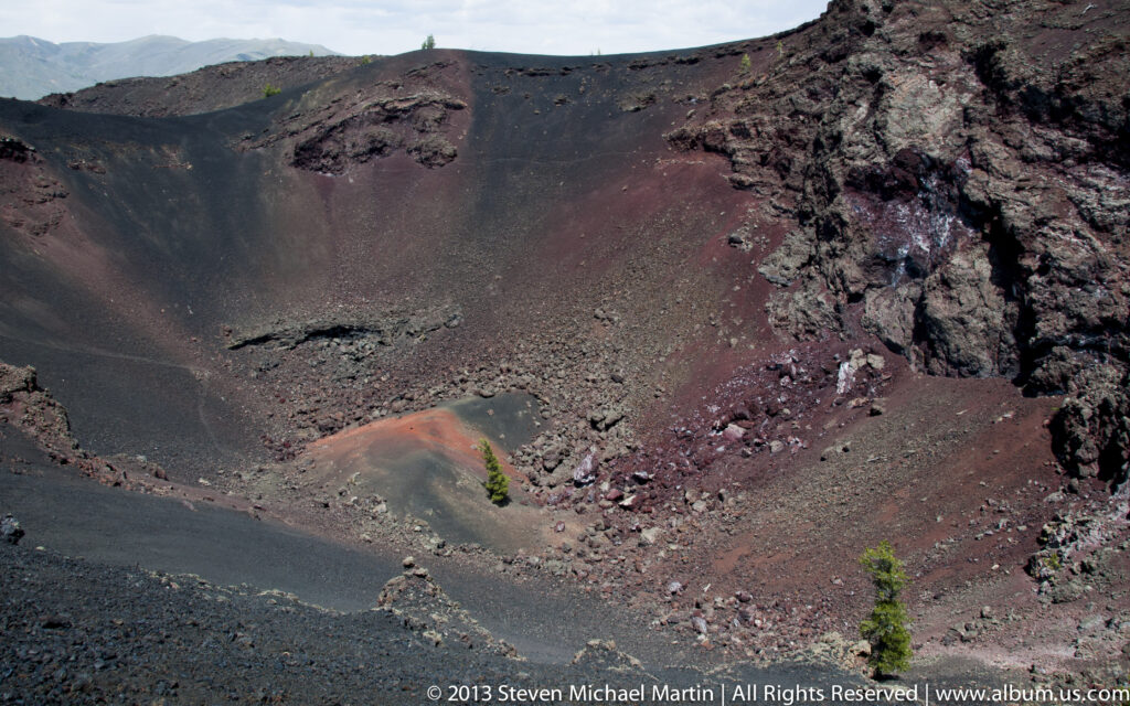 Black cinders and red-brown rock form the steep inner slope of a volcanic crater.