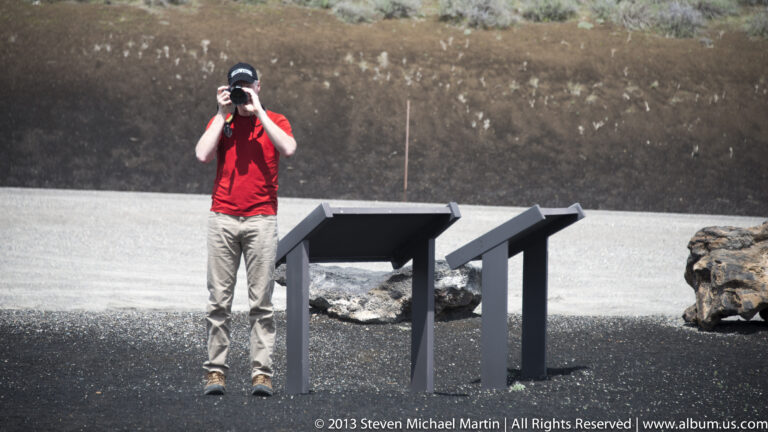 A visitor photographs beside two angled interpretive panels on a dark path.