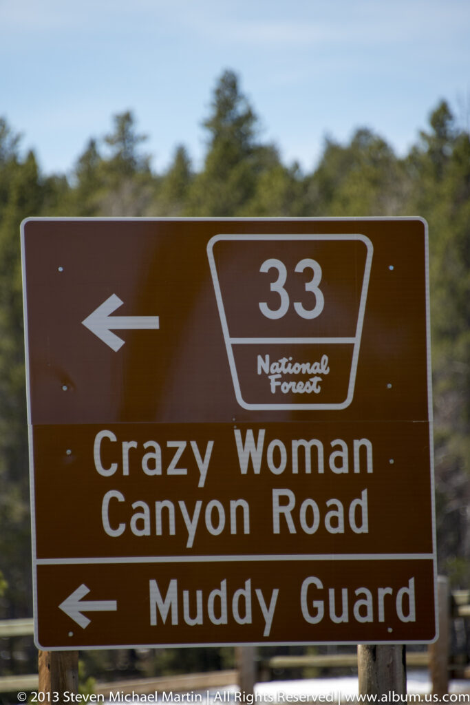 A brown sign points left to Crazy Woman Canyon Road and Muddy Guard, route 33.