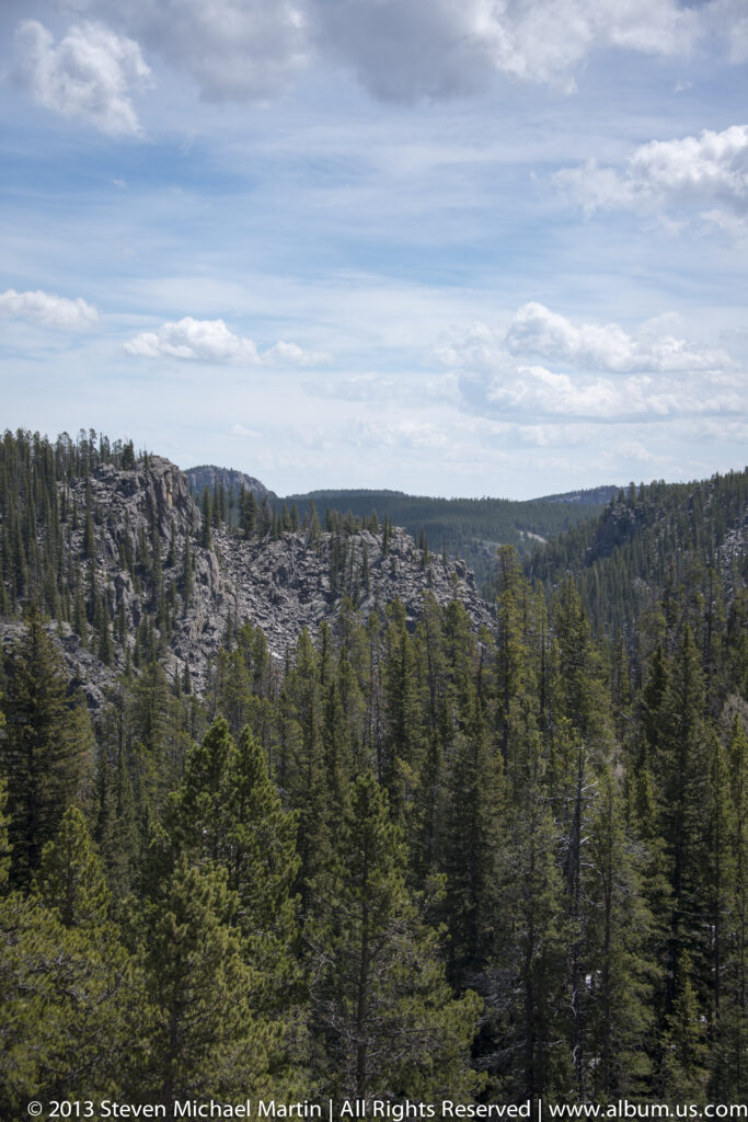 A wide view across forested canyon ridges with pale rock outcrops under layered clouds.