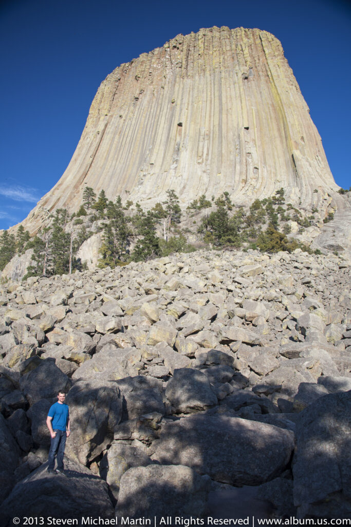 A visitor walks over pale boulders below the tall columnar face of Devils Tower.