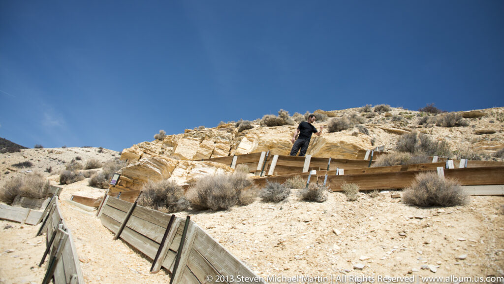 A raised walkway follows a pale hillside, where a visitor stands near the railing.