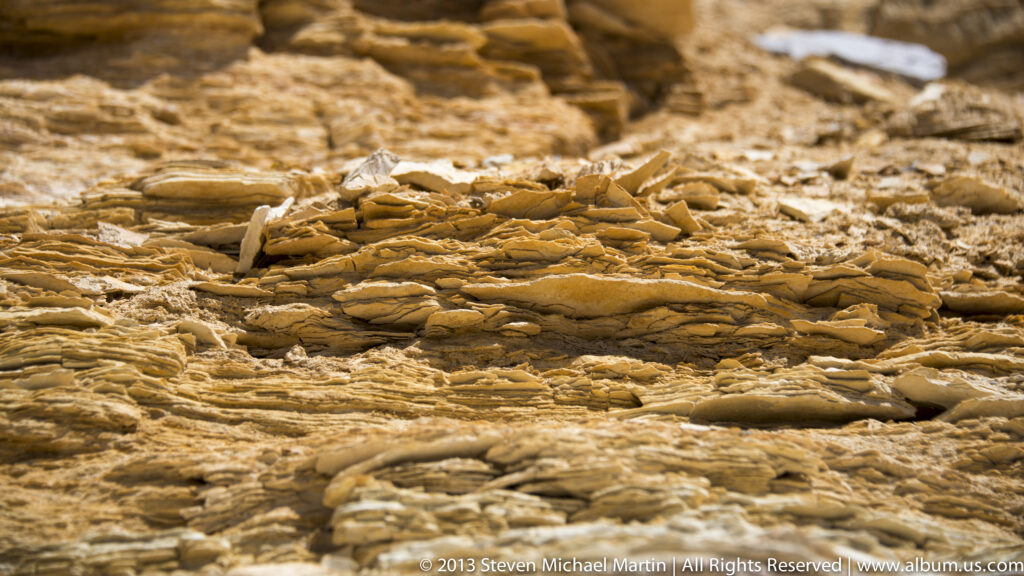 Close-set ochre and cream rock layers form a fractured, rippled surface in a tight detail view.