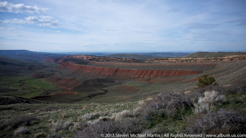 Colored sedimentary ridges and a winding road extend across a wide open basin.