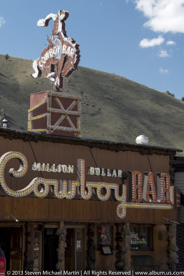 The Million Dollar Cowboy Bar sign fills a decorated western-style storefront along a town street.