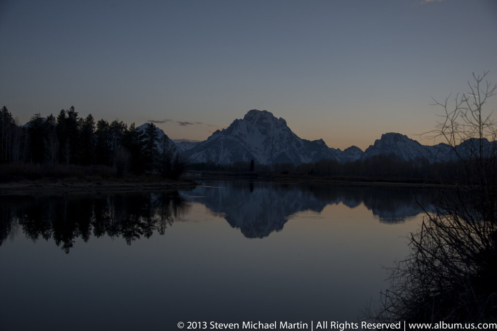 A dark mountain range and its reflection sit beneath a narrow band of twilight.