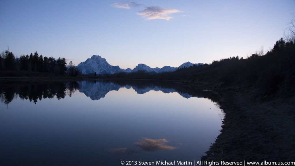 A blue and pink twilight sky and distant mountains reflect across a lake.