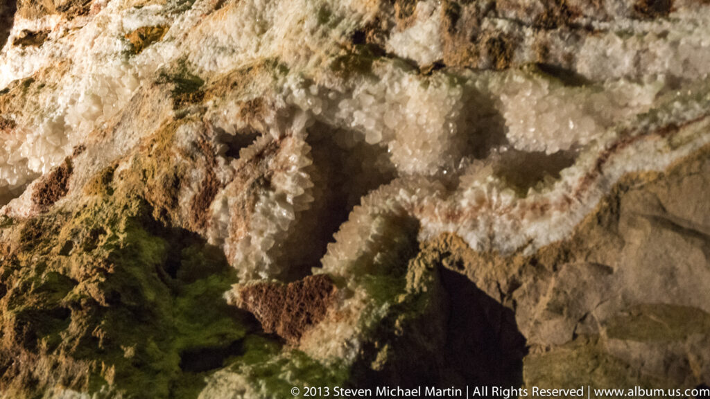 Warm light reveals pale knobby deposits and dark recesses across an uneven cave wall.