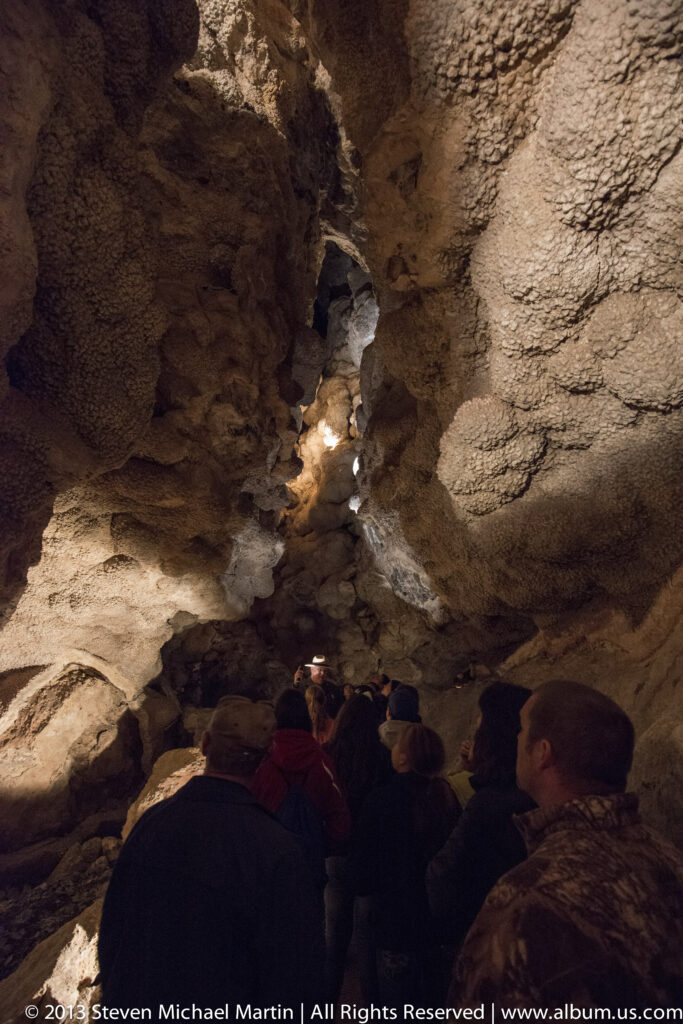 A group of visitors looks up at illuminated cave formations beneath a high ceiling.