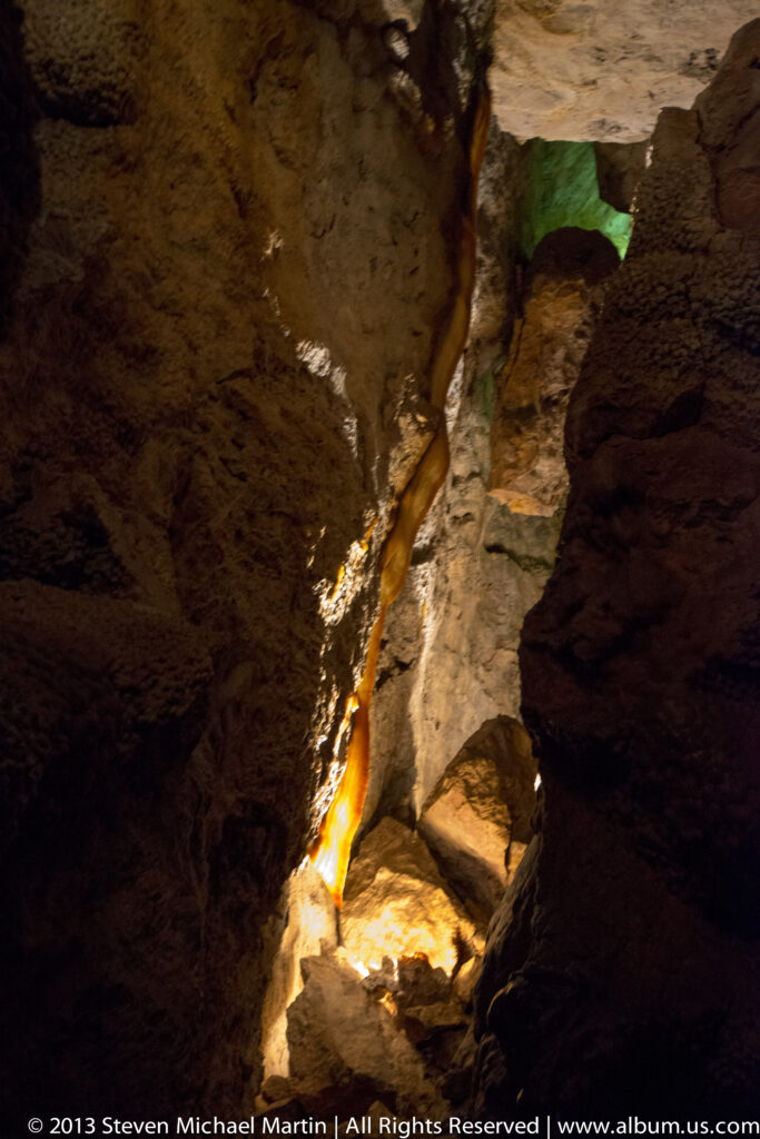 Amber light follows a narrow cave passage, with a small green-lit area above.