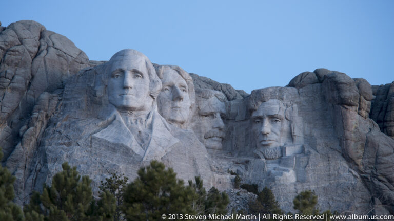 George Washington’s carved portrait dominates a close view of Mount Rushmore, with other faces extending along the ridge.