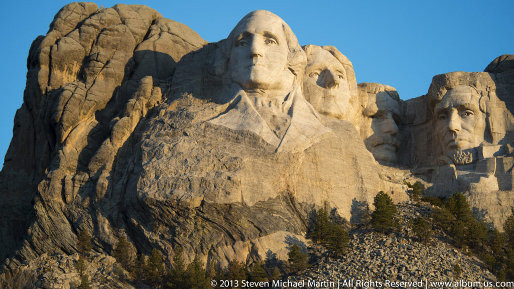 Washington’s carved portrait stands in front of Lincoln’s face on the sunlit granite ridge.