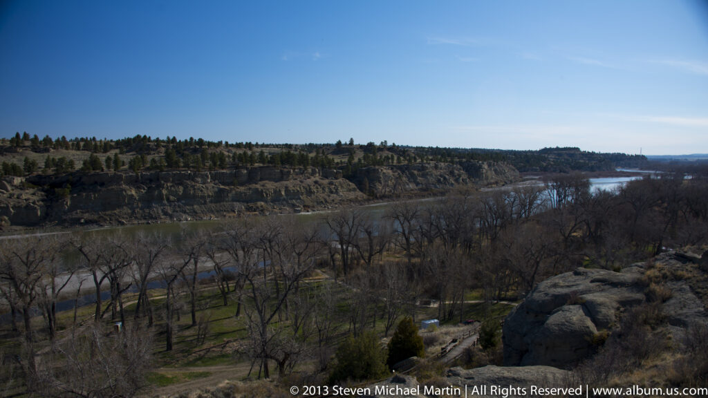 A broad river curves through a leafless wooded valley below layered sandstone bluffs.