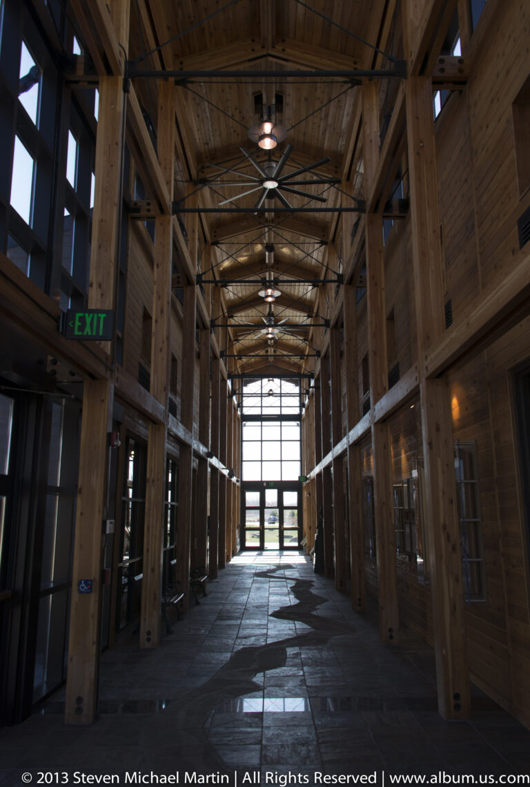 An empty timber-framed hall leads toward a bright window, with ceiling lights and an EXIT sign along the corridor.