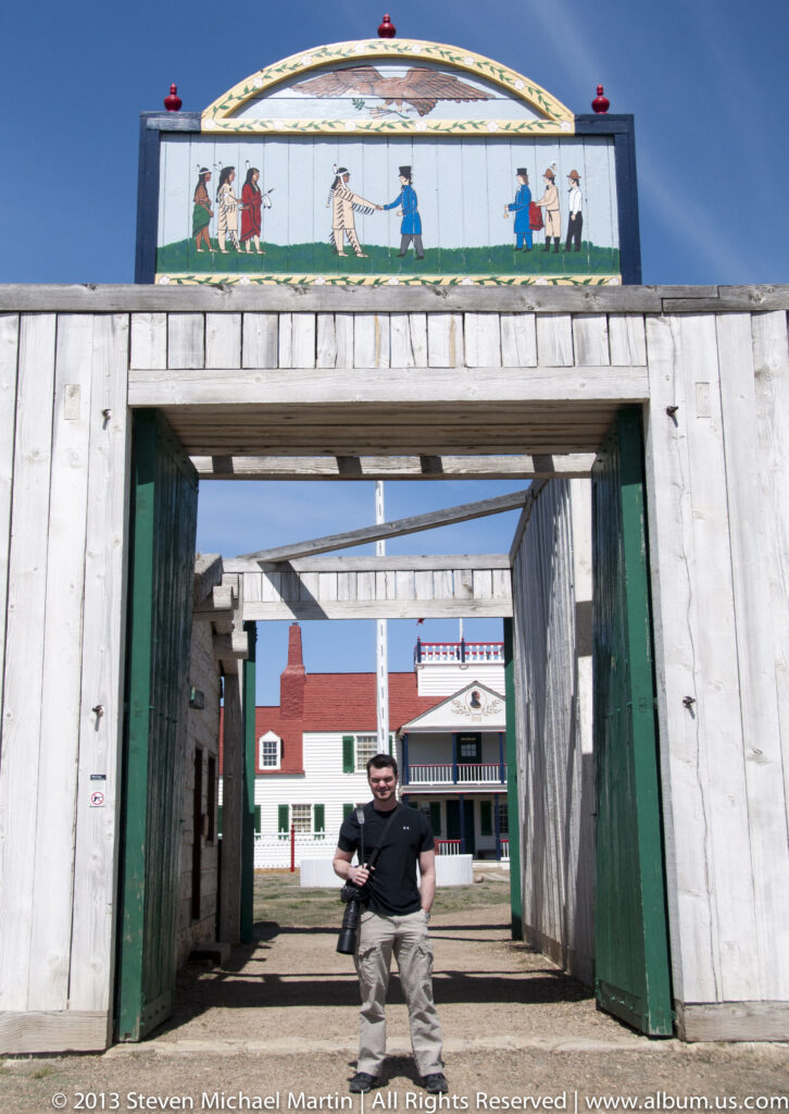 A visitor stands in a timber gateway looking through aligned entrances toward red-roofed buildings.