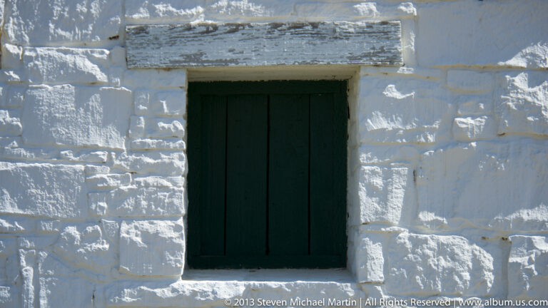 A dark green rectangular opening is recessed in a weathered white masonry wall.