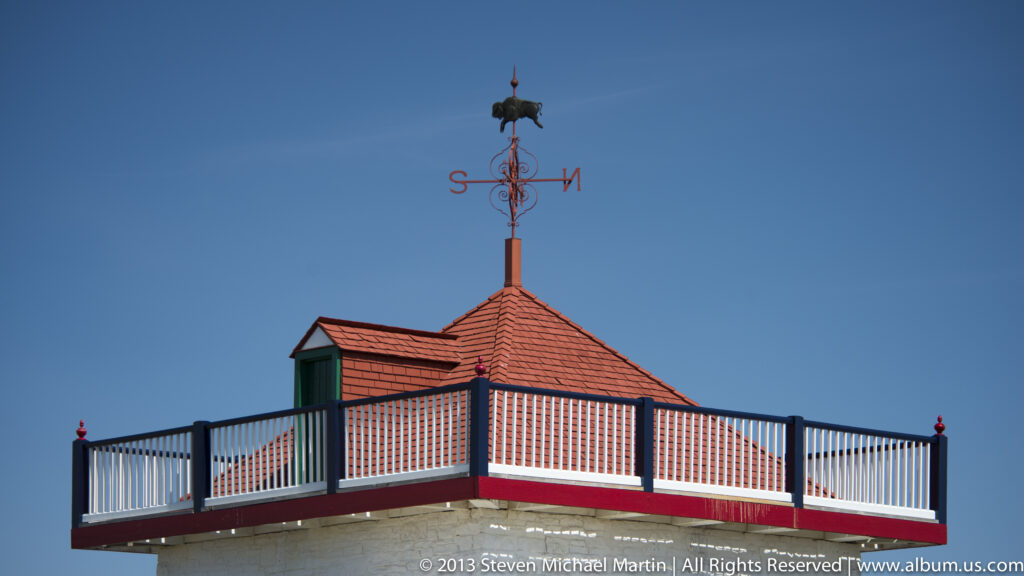 A red-roofed rooftop balcony with white railings sits below an eagle weather vane.