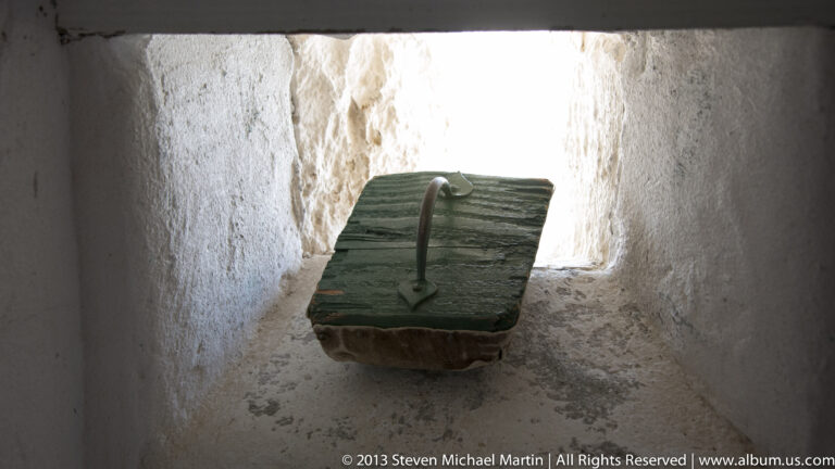 A small wooden panel with a curved handle sits on a ledge inside a deep masonry recess.