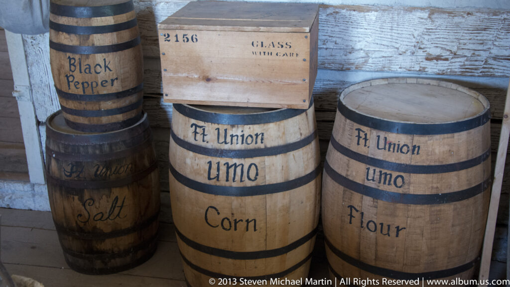 Wooden barrels labeled salt, black pepper, corn, and flour stand against a plank wall.