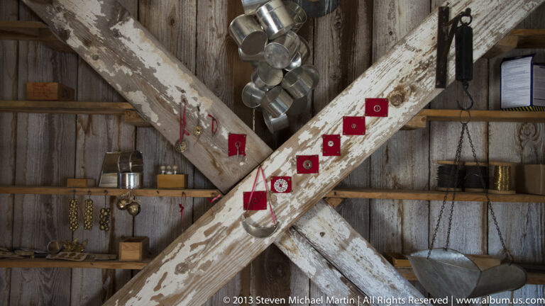 Metal cups hang from crossed beams above shelves of tools and objects.