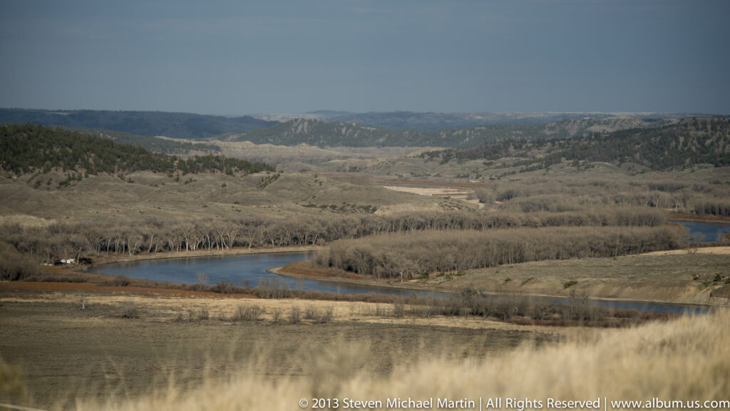 A broad Missouri River bend winds through leafless river-bottom forest and open hills.