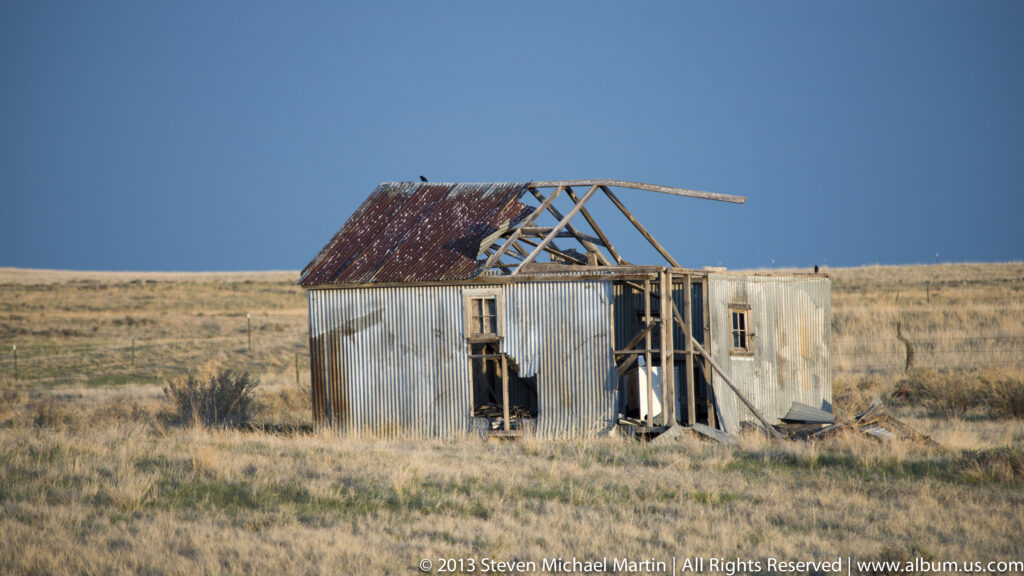 A corrugated-metal building with a partly collapsed roof stands in dry grassland.