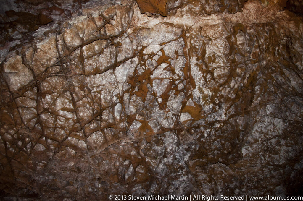 Cracked pale and rust-colored cave rock fills a close view, with seams and shallow recesses.