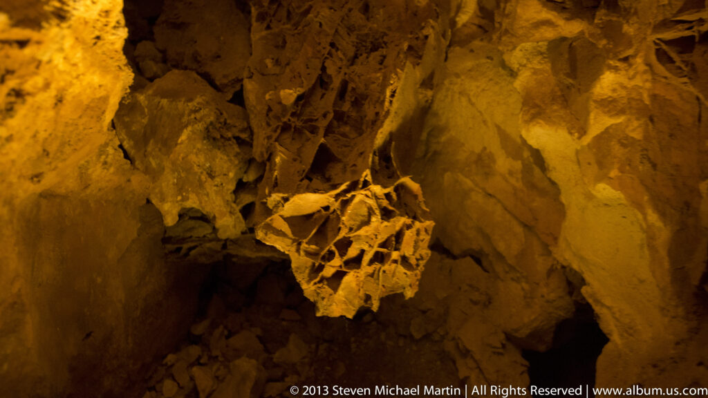 Amber light illuminates jagged cave walls around a deep, shadowed opening in the rock.