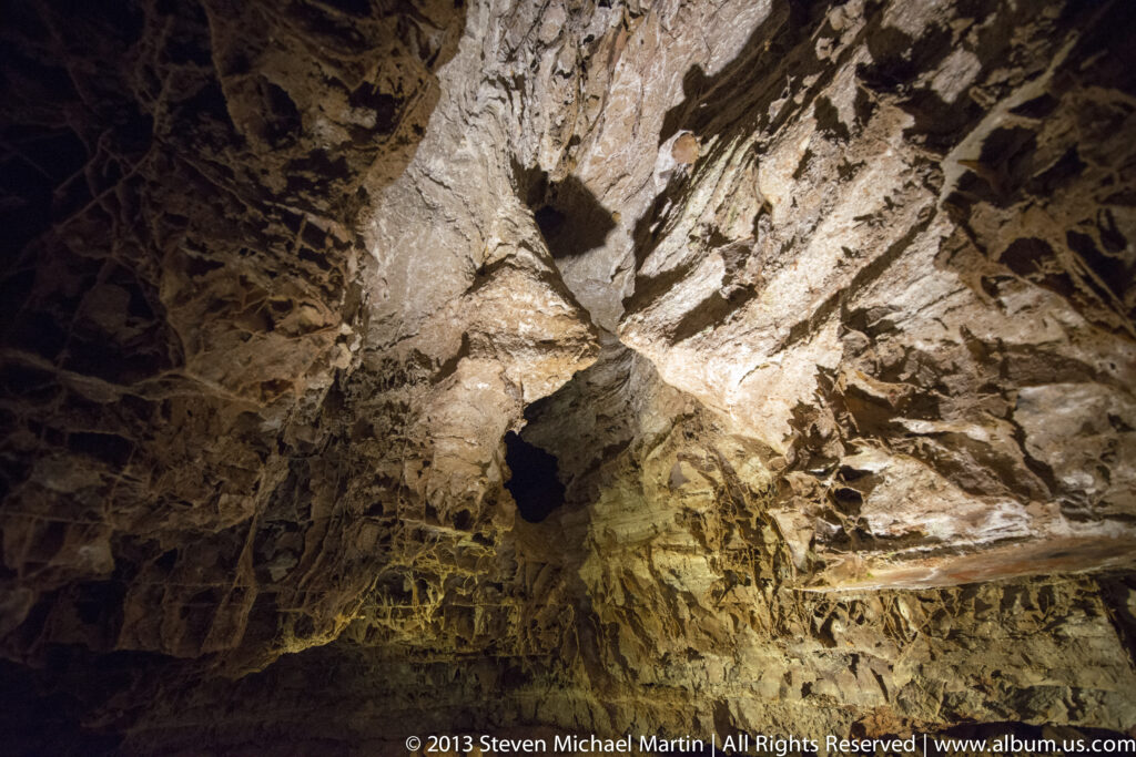 Pale, angular cave formations catch warm light against dark recesses in a close view.
