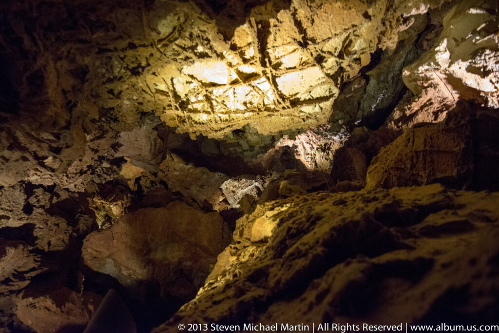 Warm light reveals irregular ledges, cracks, and recesses across a cave ceiling and wall.