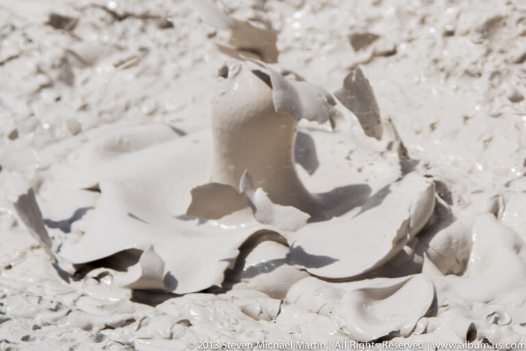 Rounded bubbles rise through a pale mud pool, forming smooth mounds and shallow hollows.