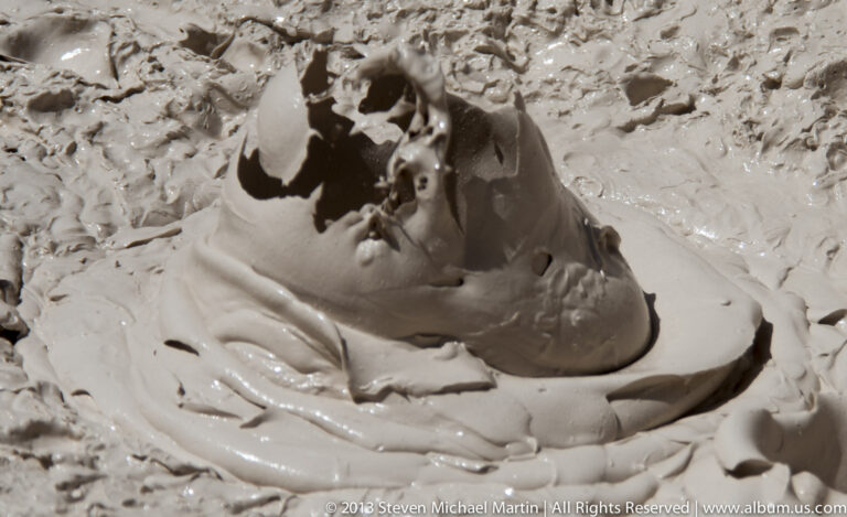 A large pale mud bubble breaks open to reveal a dark central cavity among smaller blisters.
