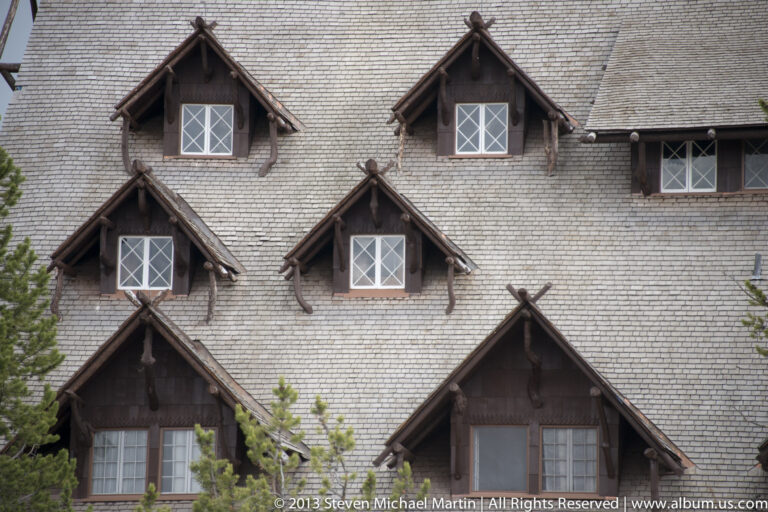 Steep gray shingles and timber dormers form a repeating pattern across a lodge roof.