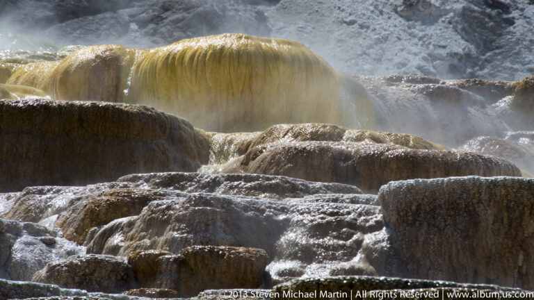 Golden thermal water spills over a travertine ledge beneath a plume of steam.
