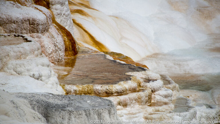 Rust-colored water channels cross pale travertine ledges and collect in shallow pools.