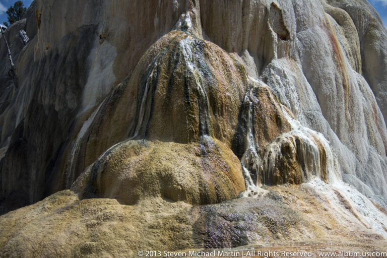 Water spills over rounded travertine mounds streaked with brown and ochre mineral deposits.