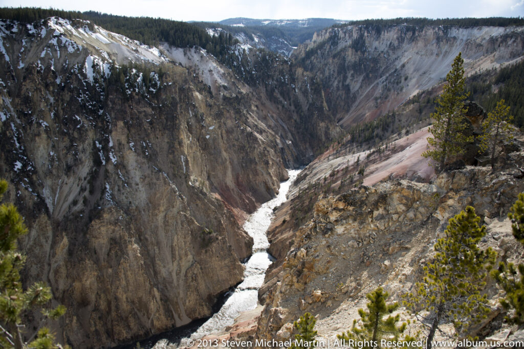 A waterfall and river descend through a deep canyon with snow-dusted rock walls.