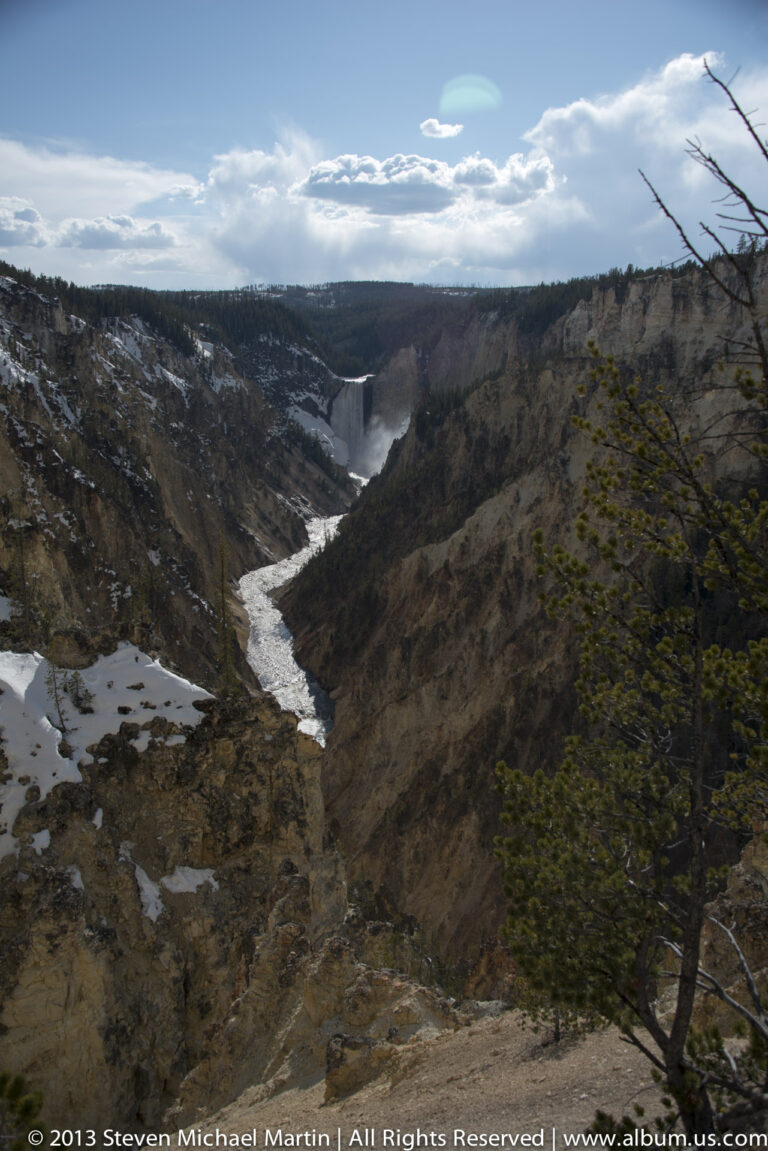 A distant waterfall lies along a pale river winding through a broad canyon.
