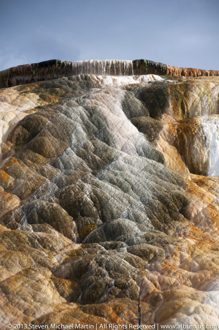Close view of rippled travertine with white, gray, ochre, and rust-colored bands running across the frame.