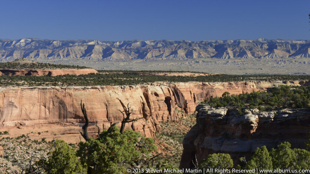 A pale layered cliff spans the middle distance below a broad mesa and above a scrub-covered foreground.