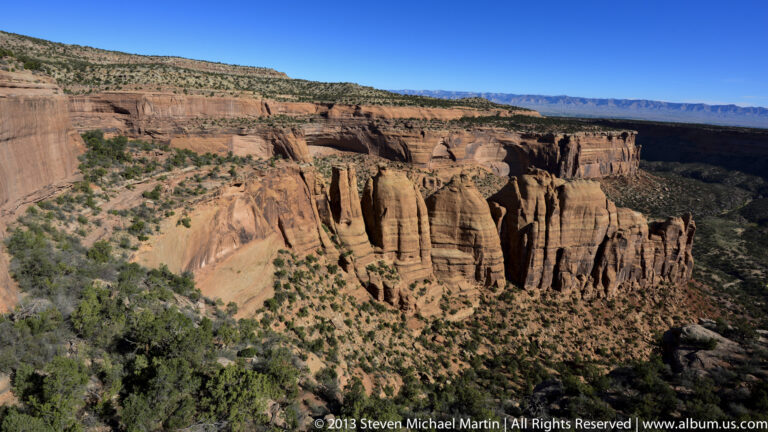 Narrow rock fins and deep ravines cut through a red-rock canyon below a distant plateau.