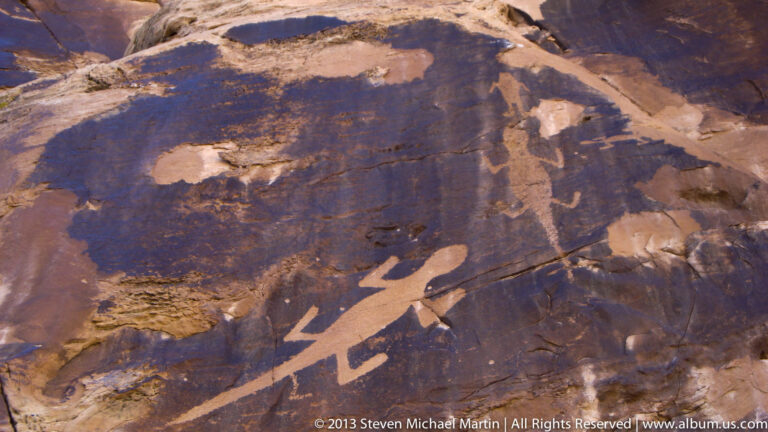 Dark pictorial markings and pale outlined motifs cover a sloping sandstone surface.