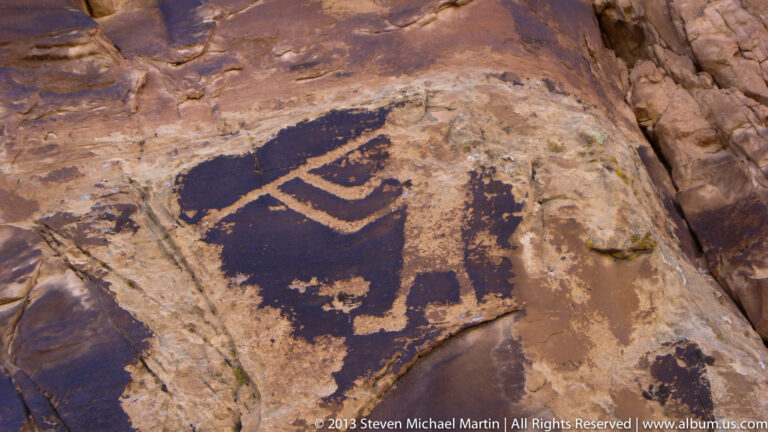 A dark quadruped-like figure appears on pale sandstone beside other faint markings.