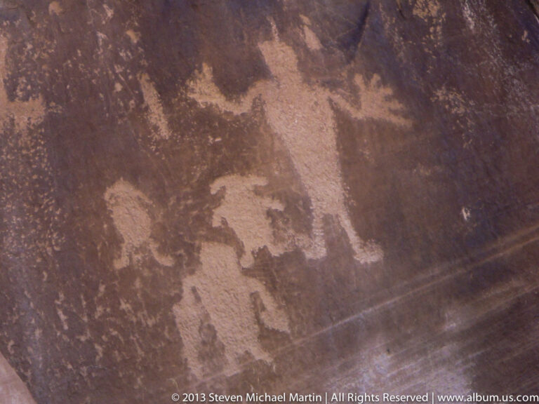 Faint irregular dark markings cross a weathered reddish sandstone wall in a close view.
