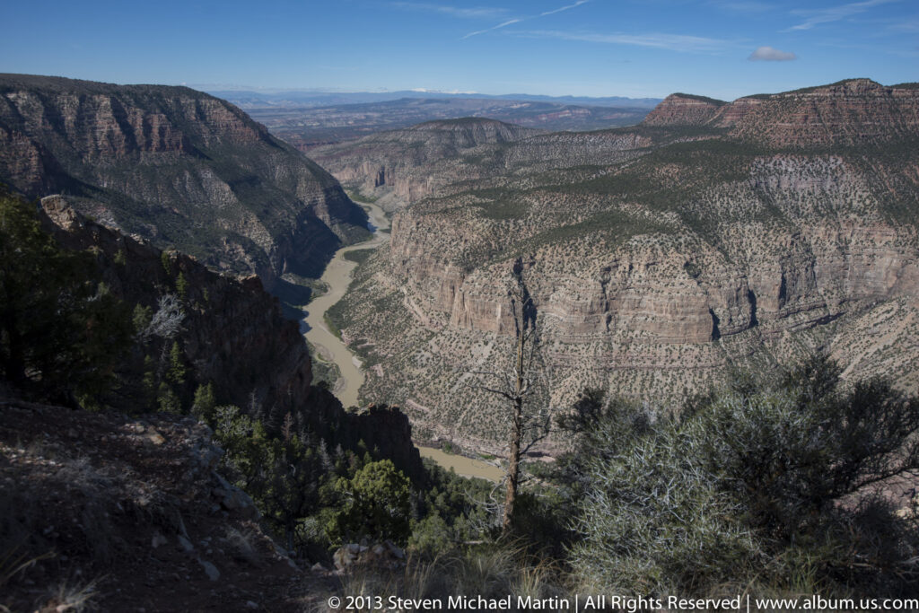 A winding river runs through a broad canyon beneath layered walls and distant mesas.